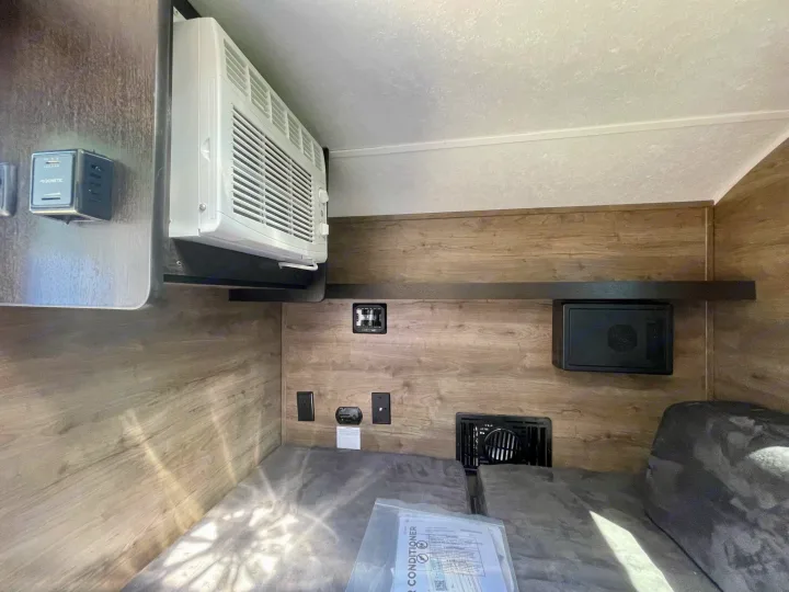 RV rental interior showing AC unit, Dometic controls, outlets, and a compact sleeping area with wood-paneled walls.. Braxton Creek Bushwhacker 2021