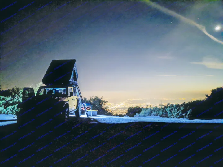 Night camping with an RV rental: a Jeep with a rooftop tent overlooks city lights under a starry sky with the moon & a contrail.. Jeep Wrangler Unlimited Rubicon 2020