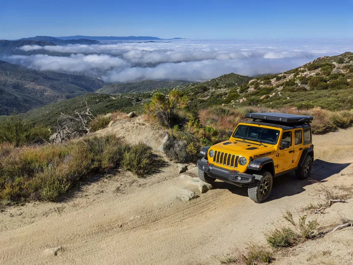 Yellow Jeep Rubicon with rooftop tent on a mountain trail overlooking clouds. Consider an RV rental for views like this!. Jeep Wrangler Unlimited Rubicon 2020