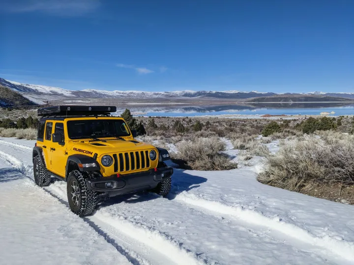 Bright yellow Jeep Rubicon on a snowy trail beside a reflective lake with mountains.. Jeep Wrangler Unlimited Rubicon 2020