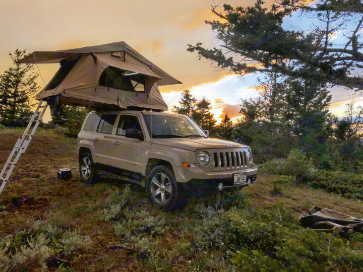 Golden hour camping: a Jeep with a rooftop tent deployed, offering a unique RV rental outdoor adventure.. Jeep Patriot 2016