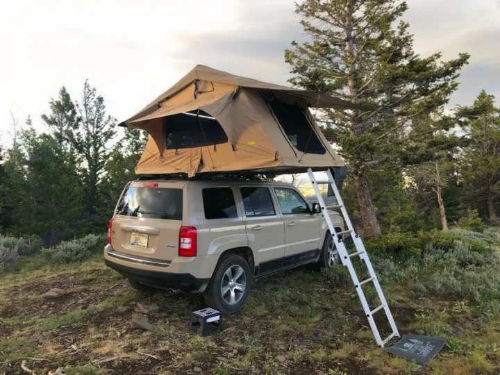 This RV rental alternative features a tan SUV with a deployed roof-top tent and ladder for wilderness camping.. Jeep Patriot 2016