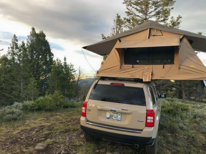 Jeep Patriot with a rooftop tent deployed in a scenic, forested mountain setting. A unique off-grid alternative to traditional RV rental for nature lovers.. Jeep Patriot 2016