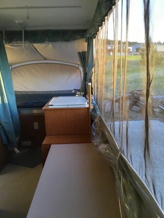Inside this RV rental, a compact kitchen with sink, a cozy bed, and screened windows showcasing outdoor views.. Coleman Fairlake 2002
