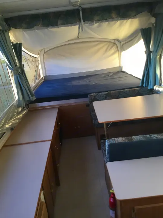 Cozy rv rental: a pop-up camper interior with canvas walls, a bed, and a compact dinette with wood storage.. Coleman Fairlake 2002