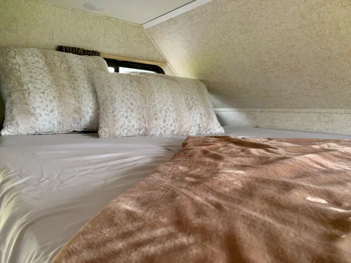 Cozy RV rental bedroom with soft, light-colored bedding and fluffy pillows, offering a comfortable space for travel.. Forest River Sunseeker 2018