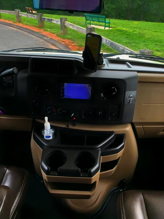 RV rental dashboard featuring a backup camera, phone mount, and hand sanitizer, with an outside view of a park.. Forest River Sunseeker 2018