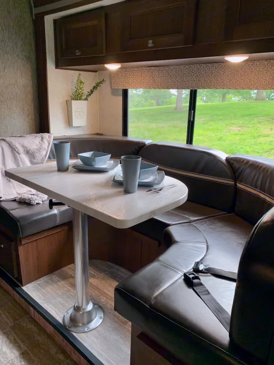 RV rental dinette with U-shaped leatherette seating, set table, and scenic window view. Ideal for travel trailer or motorhome trips.. Forest River Sunseeker 2018