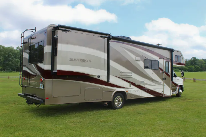 Modern Class C RV rental, Sunseeker brand, tan/maroon colors, slide-out extended, parked on green grass.. Forest River Sunseeker 2018