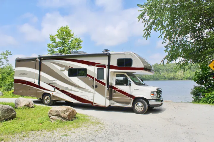 This Sunseeker RV rental is parked by a scenic lake, perfect for outdoor adventures and nature getaways.. Forest River Sunseeker 2018