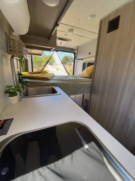 RV rental interior: cozy bed, kitchen with sink & stovetop, and outdoor view. Ideal for van life adventures!. Winnebago Other 2022