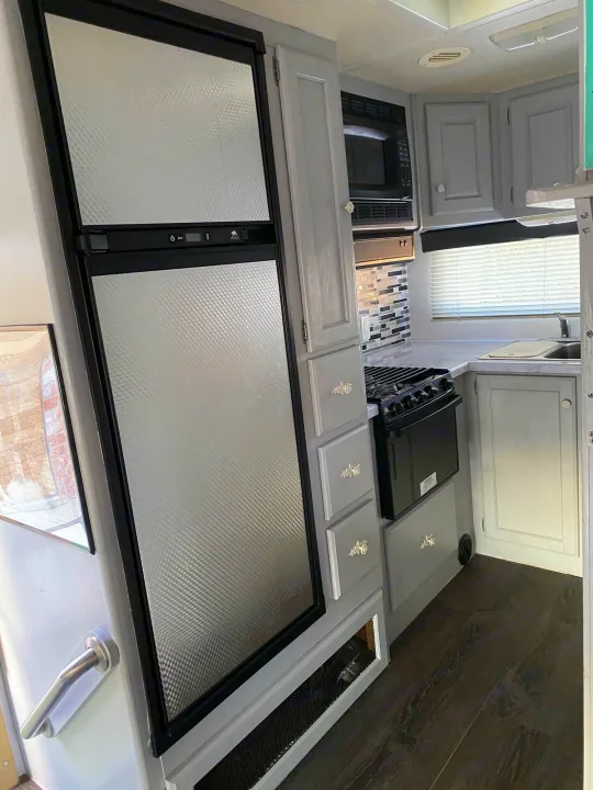 Step inside this well-equipped RV rental kitchen featuring a refrigerator, stove, microwave, and sink with gray cabinets.. Holiday Rambler Atlantis 2002