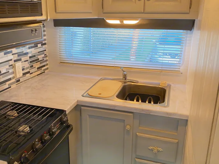 Inside an rv rental: a bright, updated kitchenette with marble-look countertops, sink, and cooktop. Perfect for road trips.. Holiday Rambler Atlantis 2002