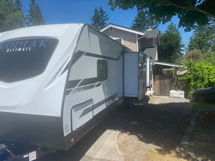 Kodiak Ultimate RV rental, a white travel trailer with its slide-out extended, parked in a sunny residential driveway.. Dutchmen Kodiak 2021