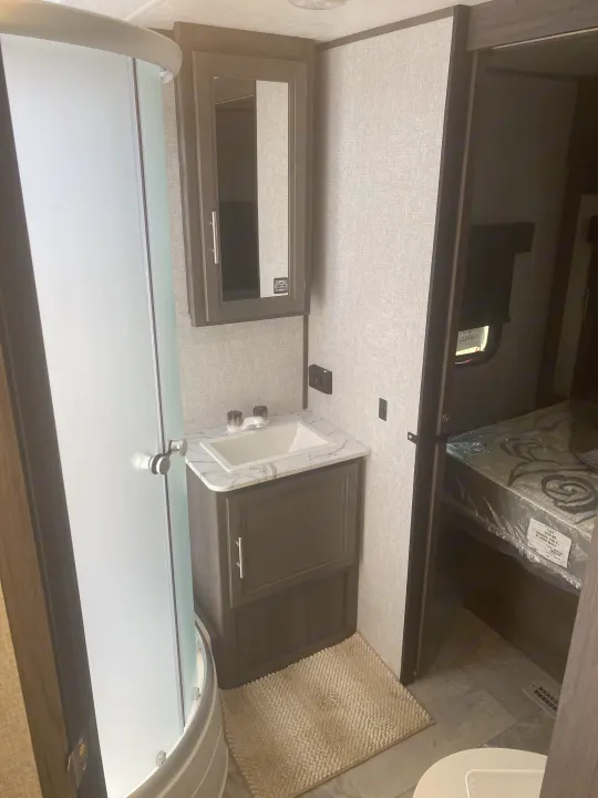 RV rental bathroom with a modern corner shower, vanity, sink, and mirrored medicine cabinet, next to a bedroom.. Dutchmen Kodiak 2021