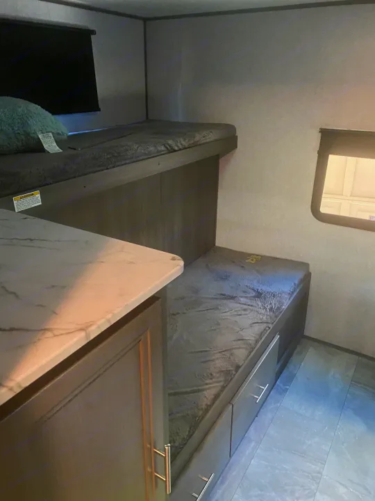 This RV rental interior features two bunk beds with a pillow, under-bunk storage drawers, and a window, creating a cozy sleeping area.. Dutchmen Kodiak 2021