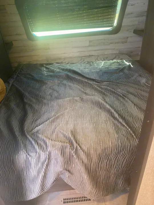 Cozy RV rental bedroom featuring a dark, textured comforter, window with blinds, and wood-paneled walls.. Dutchmen Kodiak 2021