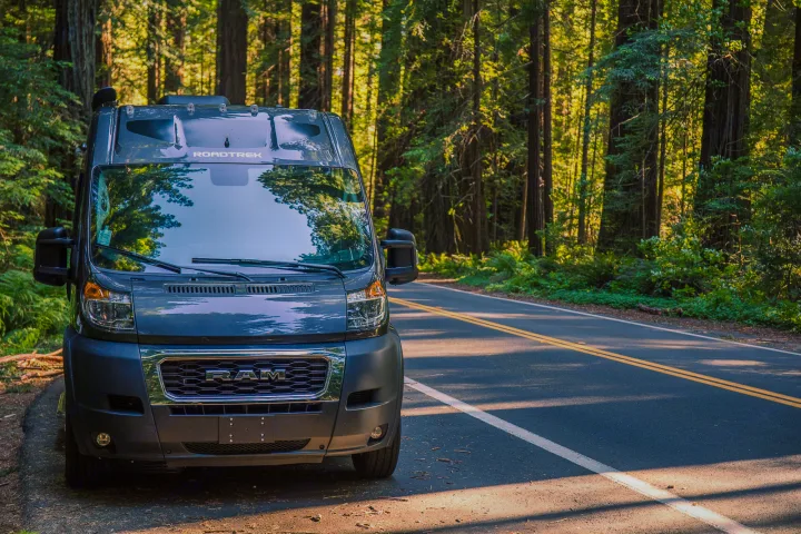 Gray Roadtrek RAM camper van RV rental parked on a forest road with tall, sunlit trees.. Roadtrek Play 2021