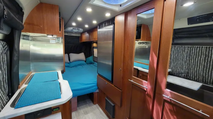 Explore this RV rental's well-designed interior: kitchen with covered sinks, comfortable bed, fridge, and stylish cabinetry.. Roadtrek Play 2021