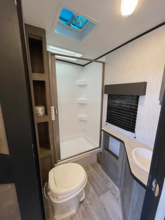 Clean, modern RV rental bathroom: features a toilet, standing shower, sink vanity, and integrated storage shelves.. Heartland North Trail 2021