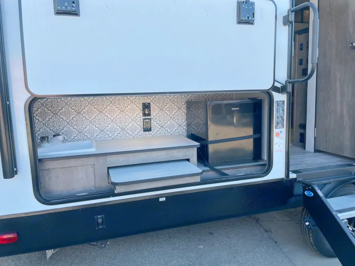 RV rental with an outdoor kitchen, featuring a sink, counter, and Hotpoint mini-fridge for camping convenience.. Heartland North Trail 2021