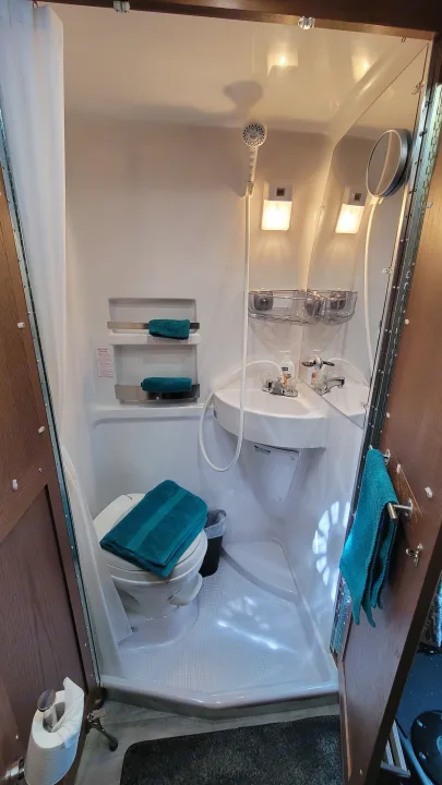 This RV rental's compact bathroom features a shower, toilet, and sink. Towels and mirror are visible, showing efficient use of space.. Roadtrek Play 2021