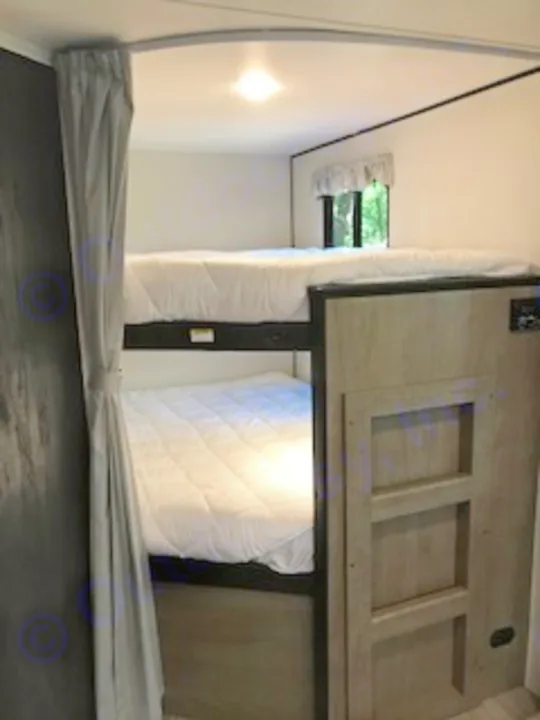 Comfortable bunk beds within an RV rental, featuring bright lighting, a window, and overhead storage.. Keystone Hideout 2021