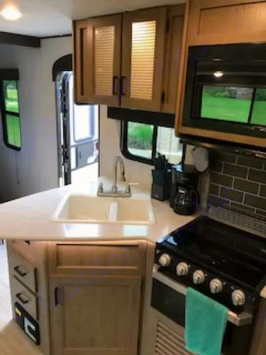 Modern RV rental kitchen interior: features a double sink, microwave, stove, and coffee maker, ready for your road trip adventures.. Keystone Hideout 2021