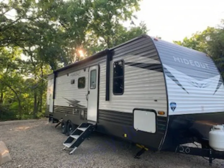 A modern black and white travel trailer RV rental is parked on a gravel site, ready for a serene outdoor adventure in nature.. Keystone Hideout 2021