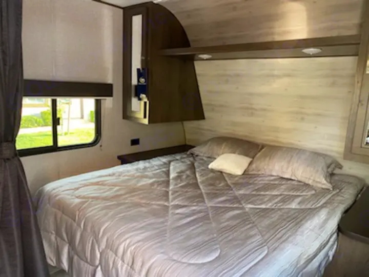 Explore the comfortable RV rental bedroom, featuring a queen-sized bed, window, and built-in storage.. Jayco qbw 2021