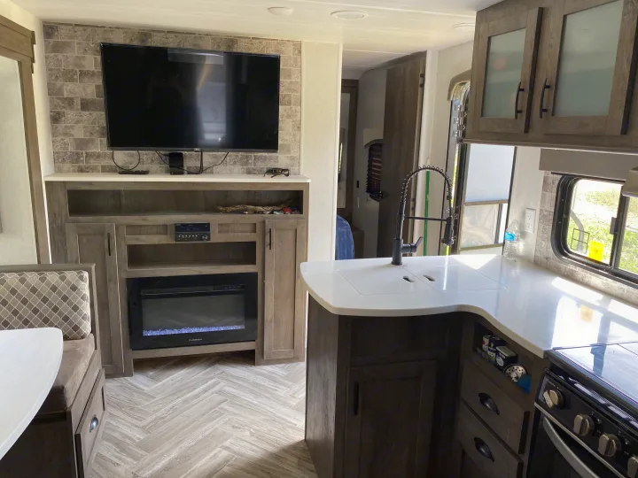 Modern RV rental interior showing living area with TV, electric fireplace, and kitchen with dinette.. Forest River Evo 2020