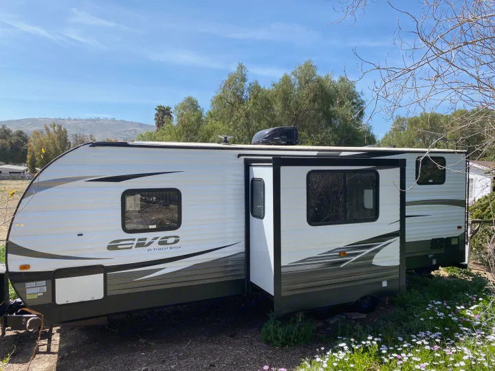 This white and dark grey travel trailer, an excellent RV rental, features a visible slide-out and Dometic AC for comfort.. Forest River Evo 2020