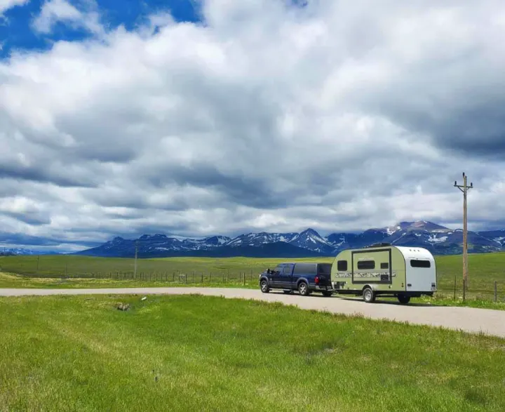 Scenic **rv rental** & truck parked by a field, with snow-capped mountains under a cloudy sky. Ideal for a mountain road trip.. Other Other 2018