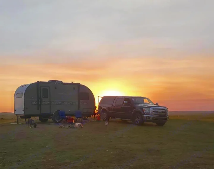 RV rental sunset camping: Travel trailer, truck, and gear in a field at dusk. A dog enjoys the serene outdoor view.. Other Other 2018