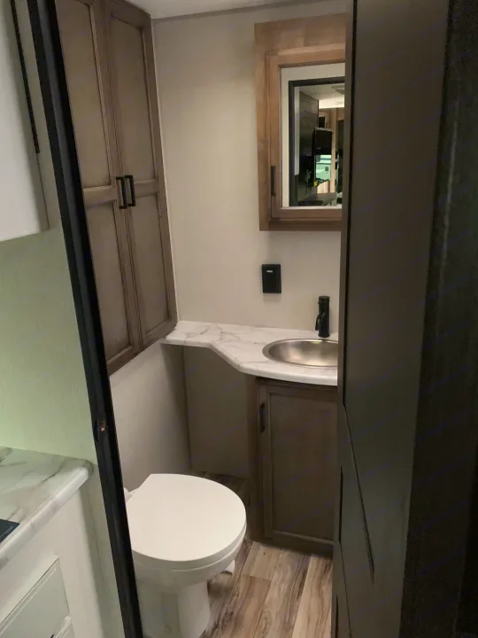 Inside a clean RV rental bathroom with toilet, sink, and cabinets. Mirrored vanity above.. Venture Rv Sporttrek 2022