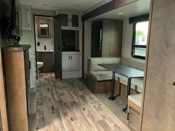 Bright RV rental interior: booth dinette, kitchen, partial bath, and wood-look flooring.. Venture Rv Sporttrek 2022