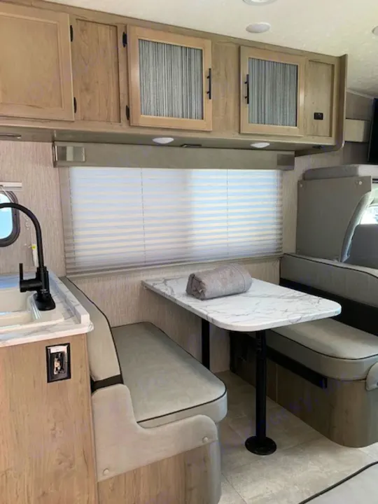 Explore this RV rental's cozy interior, featuring a dinette with a table, comfortable benches, kitchen area, and storage cabinets.. Coachmen Freelander 2021