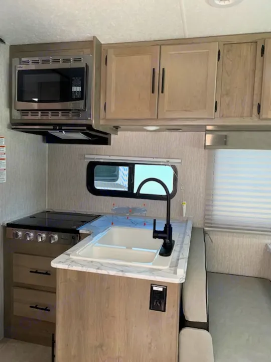 Bright RV rental interior: A functional kitchen with microwave, sink, cooktop, and storage cabinets, adjacent to seating.. Coachmen Freelander 2021