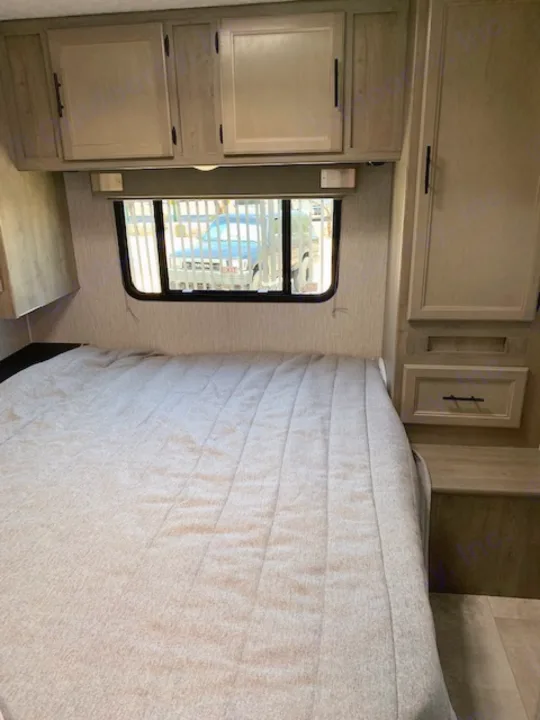 Cozy RV rental bedroom featuring a comfortable bed with light bedding, built-in wooden cabinets, and a window.. Coachmen Freelander 2021