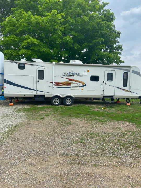 A large white Jayco Eagle Super Lite travel trailer (RV rental) parked on gravel, with green trees in the background.. Jayco Camper Trailer- Eagle 2011