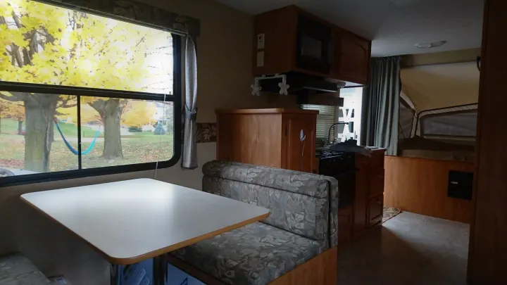 Cozy RV rental interior showcasing a dinette, kitchen, & pop-up bed, with an autumn window view.. Starcraft Travel Star 2007