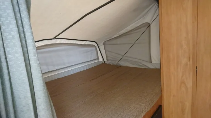 Inside an RV rental: a cozy pop-up bed area with canvas walls, comfy bedding, and light wood storage.. Starcraft Travel Star 2007