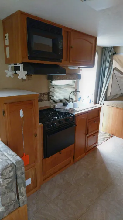 Interior of a well-equipped RV rental, featuring a kitchenette with microwave, stovetop, wooden cabinets, and dinette.. Starcraft Travel Star 2007