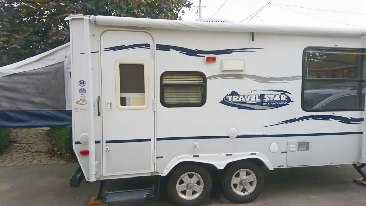 Side view of a white & grey Travel Star travel trailer RV, featuring a pop-out tent section and dual axles. Consider this for rv rental.. Starcraft Travel Star 2007