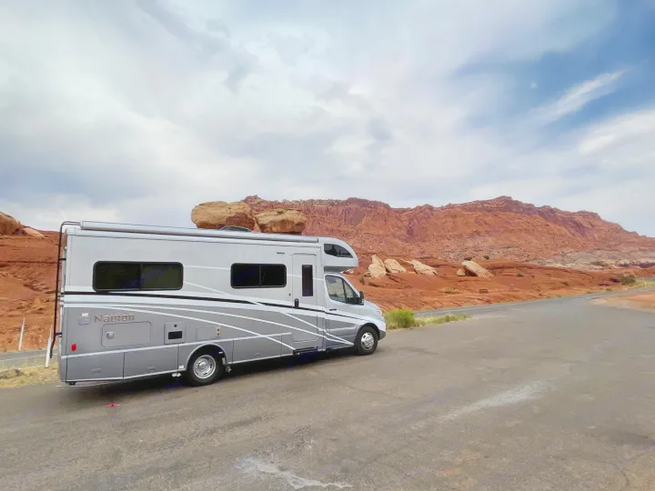 RV rental (Navion) parked at a scenic red rock desert overlook under cloudy skies. Explore the open road.. Winnebago View 2022