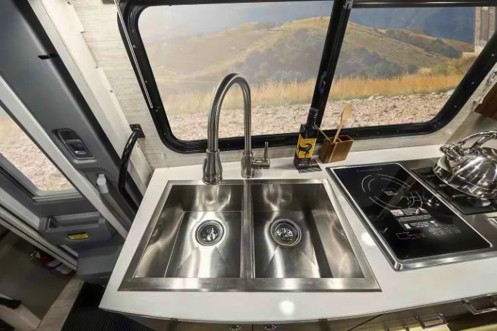 Modern RV rental kitchen with double sink, induction cooktop, and scenic window view for your travel adventure.. Winnebago View 2022