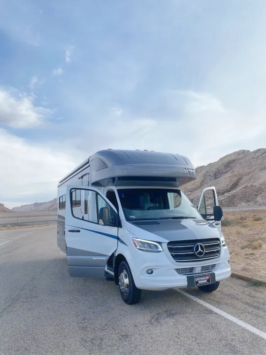White & grey Winnebago RV rental parked roadside. Driver's door open on this Mercedes-Benz Sprinter motorhome in a mountain landscape.. Winnebago View 2022