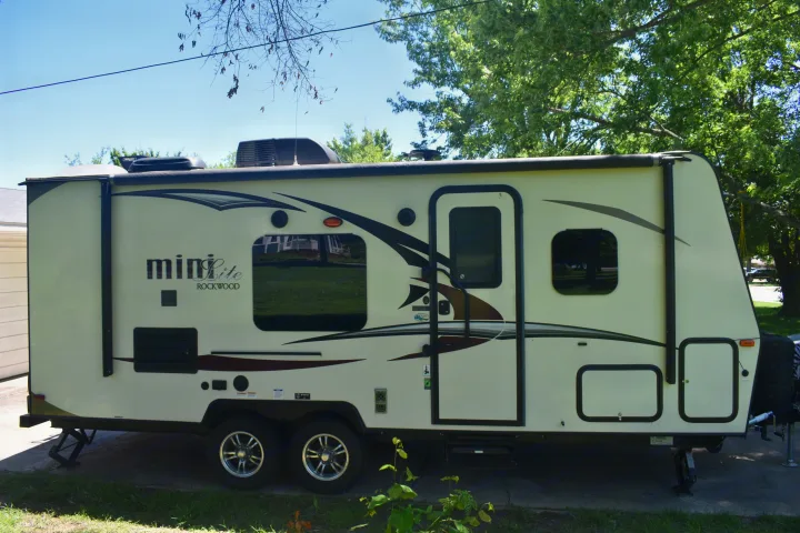 Light-colored Rockwood Mini Lite travel trailer, an RV rental, parked on concrete. Features dual axles and awning.. Forest River Rockwood Mini Lite 2017