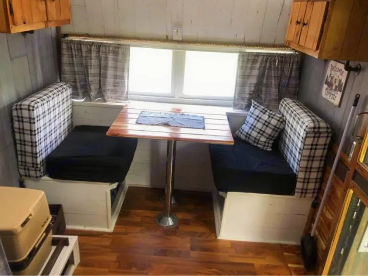 Cozy RV rental dinette with plaid benches, wood table, and window views. Perfect camper interior.. Nomad Rear fold 1962