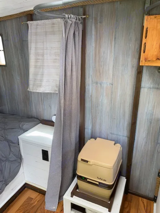Inside your RV rental: a compact layout with a portable toilet, privacy curtain, and cozy bed.. Nomad Rear fold 1962